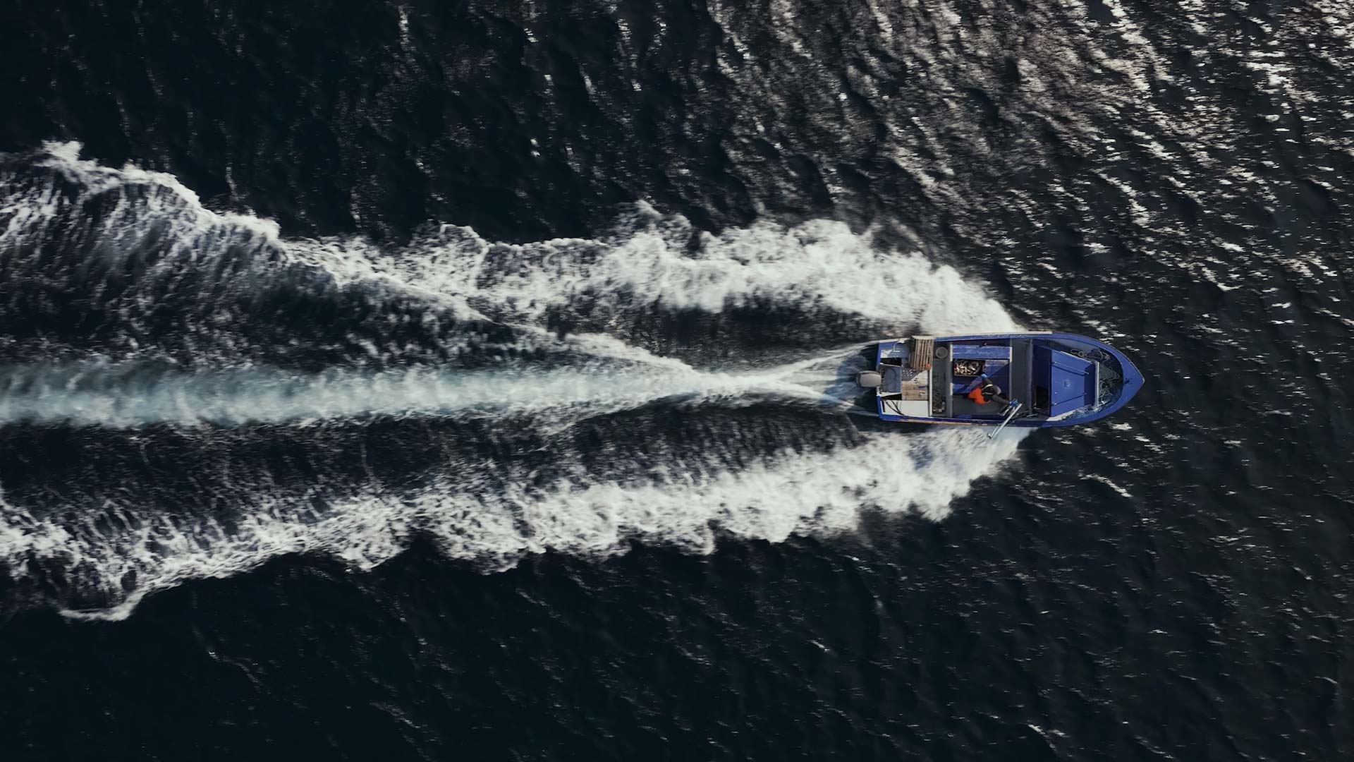 Une prise de vue aérienne symétrique par-dessus d'un petit bateau de pêche au homard se dirigeant à grande vitesse, coupant les eaux agitées.